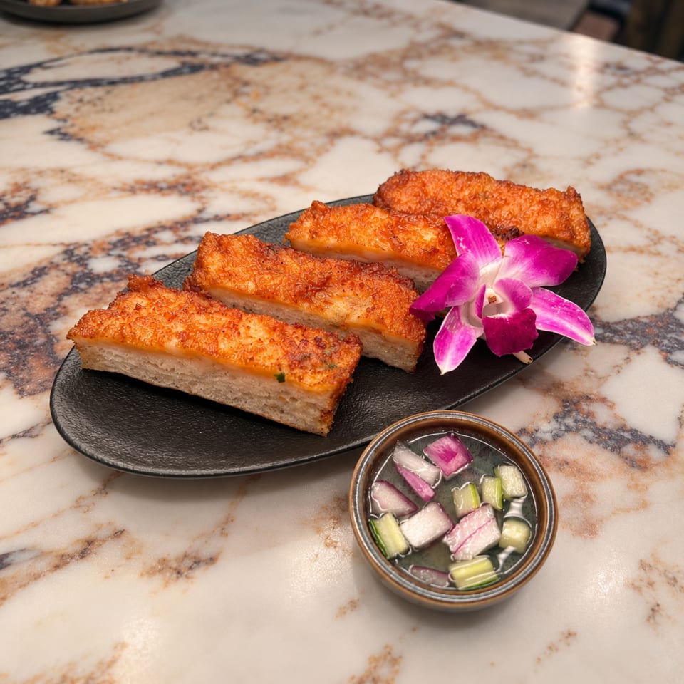 Four golden fried pastry pieces on a black plate with a purple orchid and colorful pickled vegetables on a marble table.